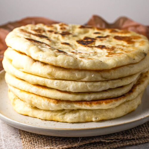 stack of greek pita bread on plate with cloth behind.