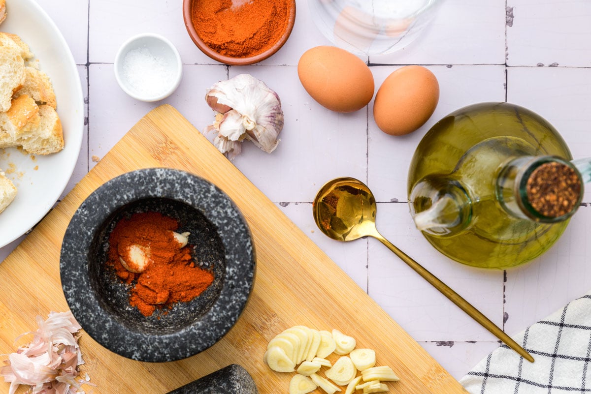 black mortar on wooden cutting board full of paprika with other ingredients around the counter.