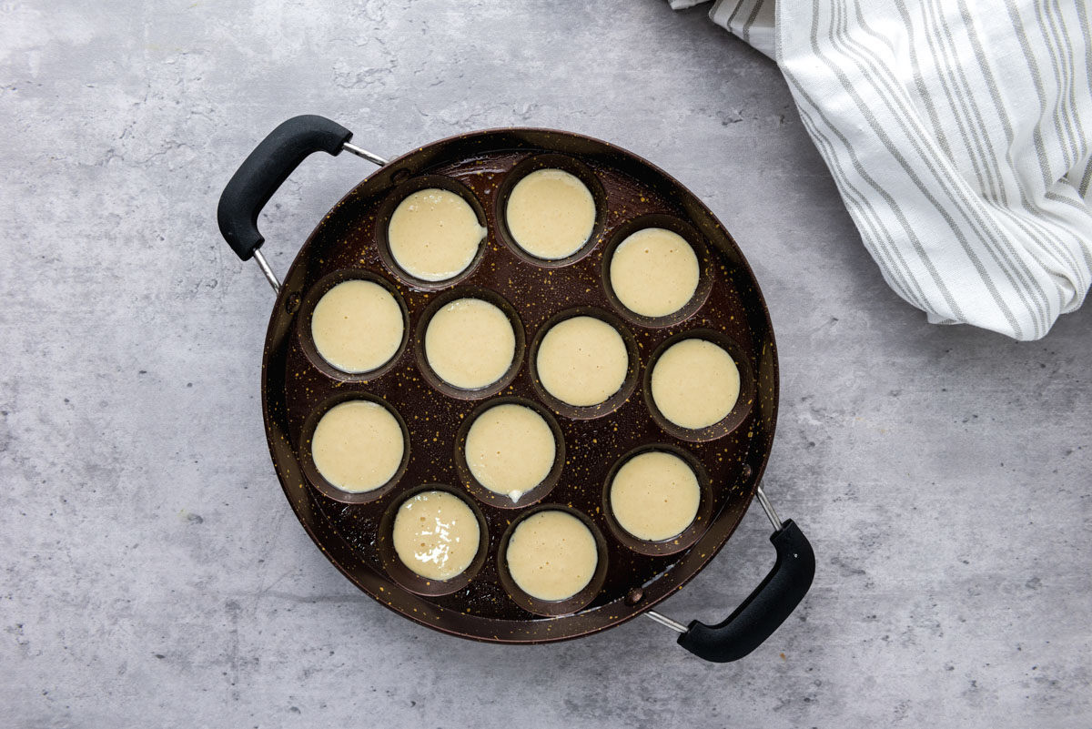 dutch mini pancakes in black cast iron pan with round holes on grey counter.