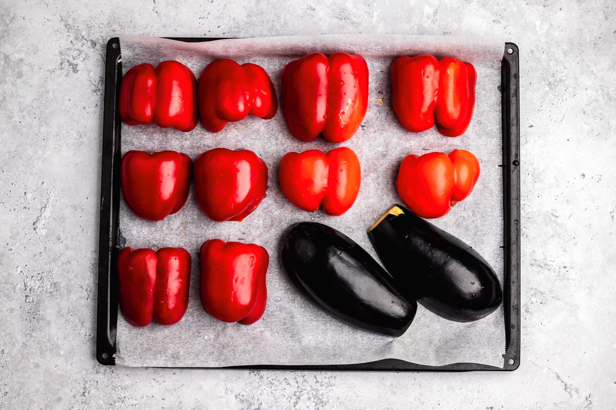red bell peppers and eggplant cut in half on parchment paper-lined baking sheet.
