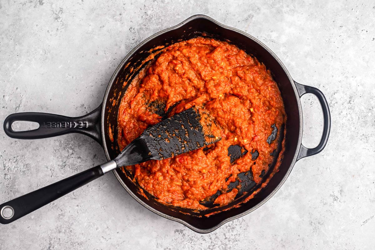 black spatula moving red pepper spread in black cast iron pan.