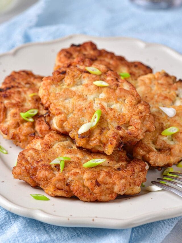 fried meat patties on white plate covered in chopped onions.