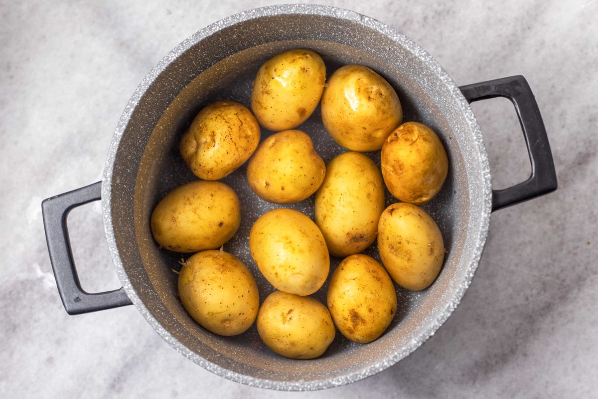 potatoes boiling in water in silver pot sitting on grey counter.