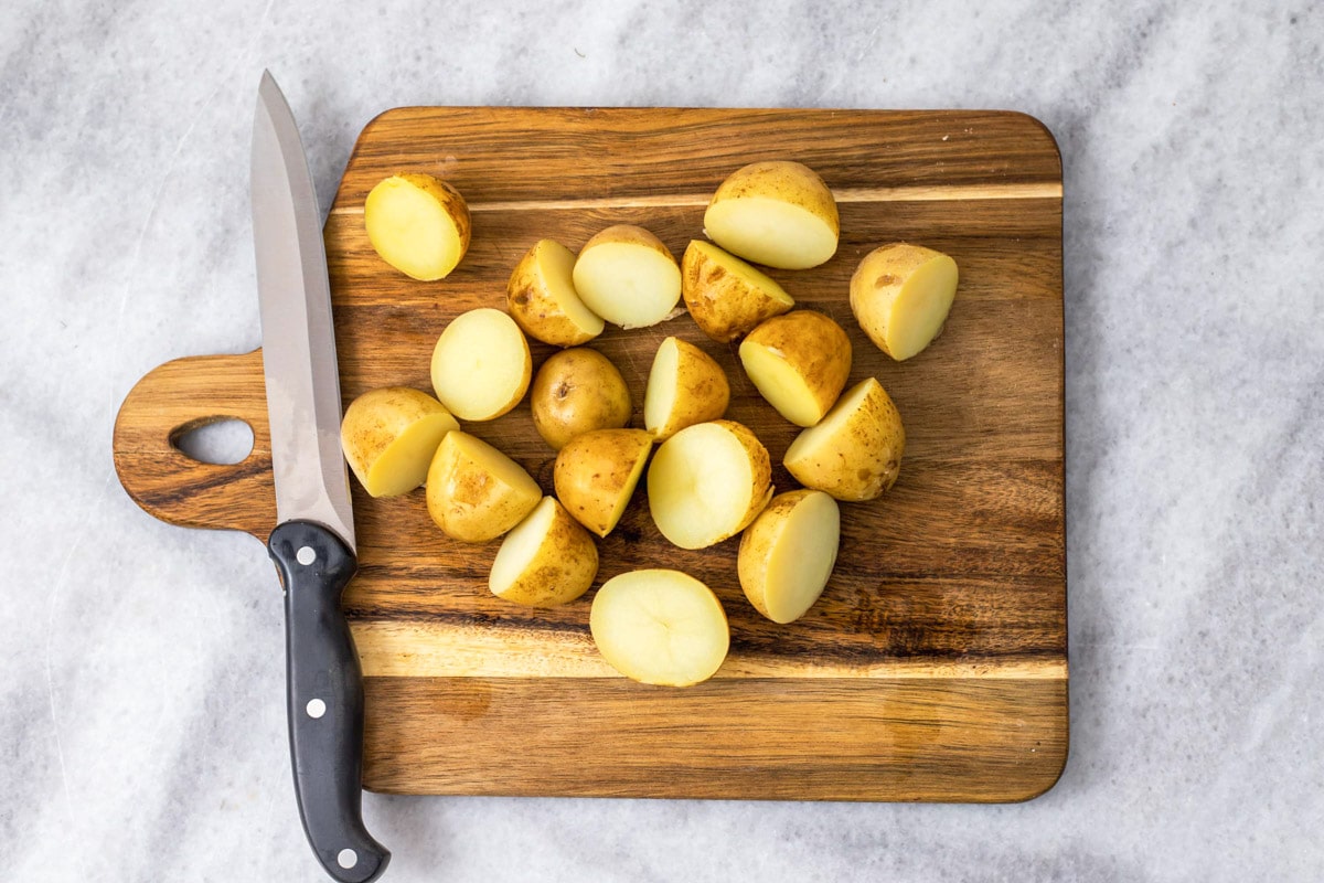 boiled potatoes cut in half on wooden cutting board with knife beside.