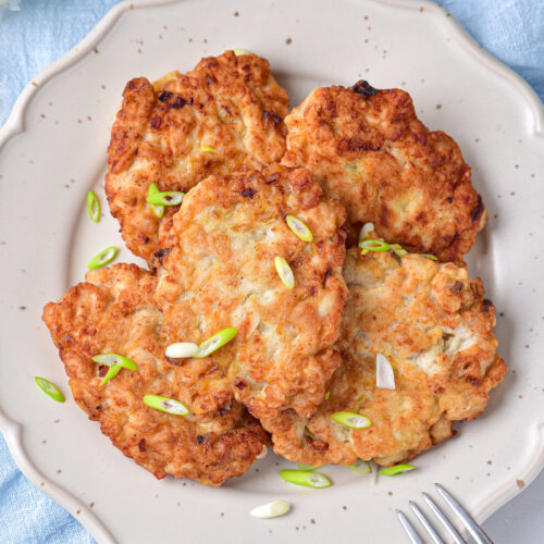 fried chicken patties with chopped onions on top sitting on white plate with blue cloth under.