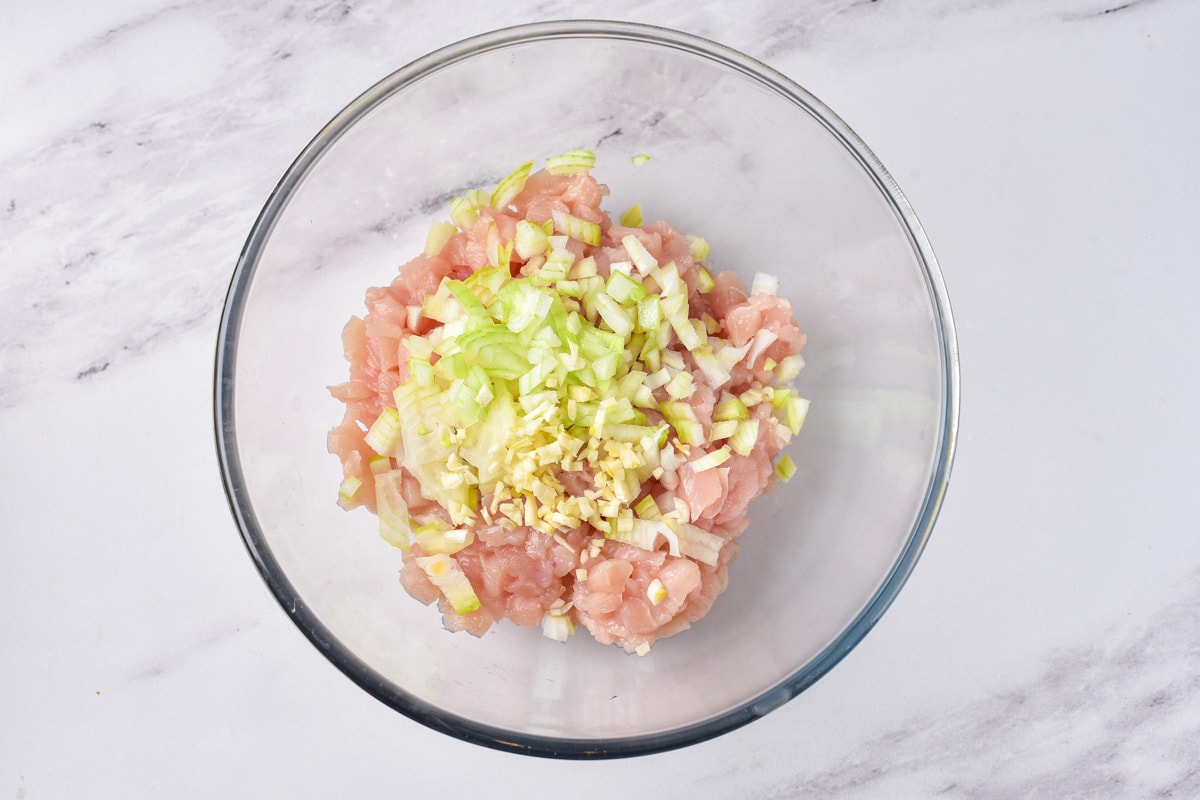 raw chopped chicken breast in clear bowl with chopped onion on top.
