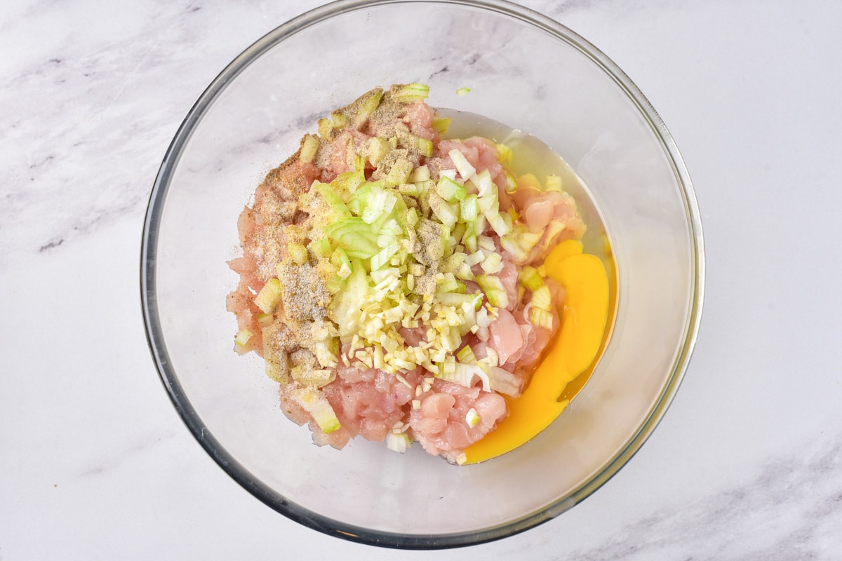 raw chicken pieces in glass bowl with raw egg and other ingredients chopped on top.