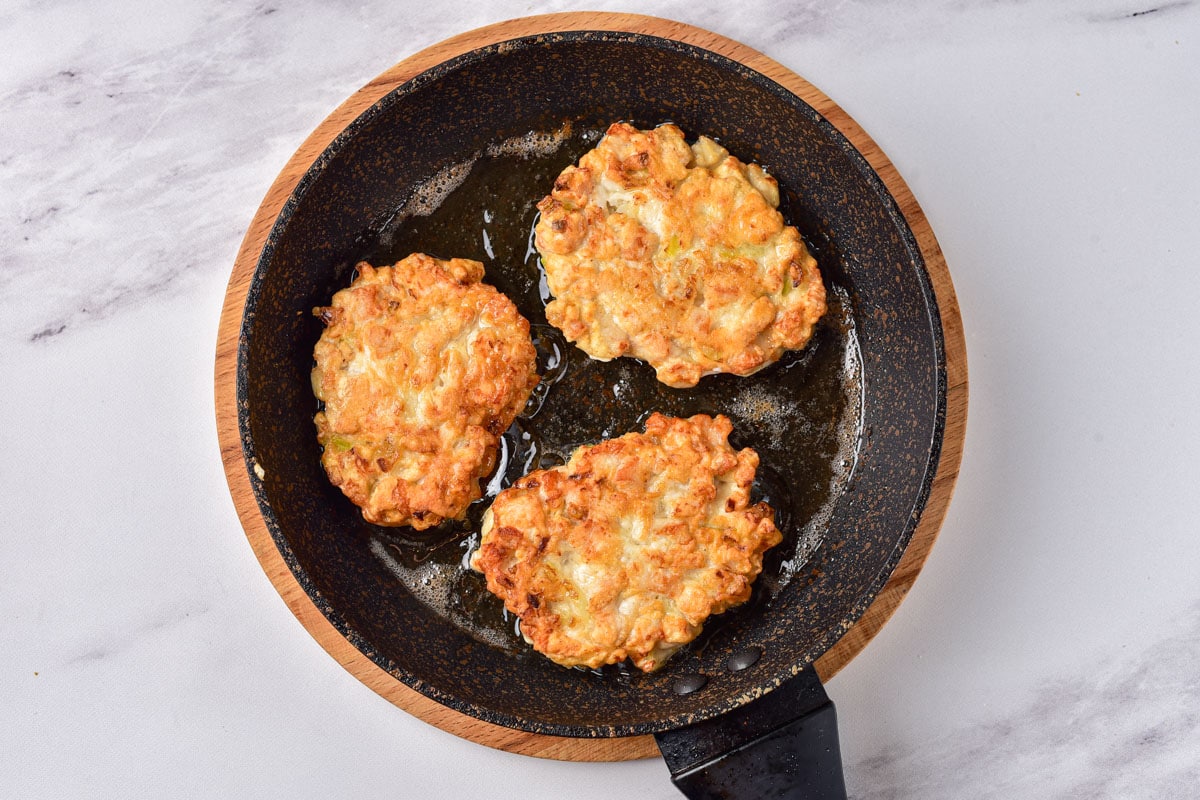 fried chicken patties in oil in black frying pan with white counter around.