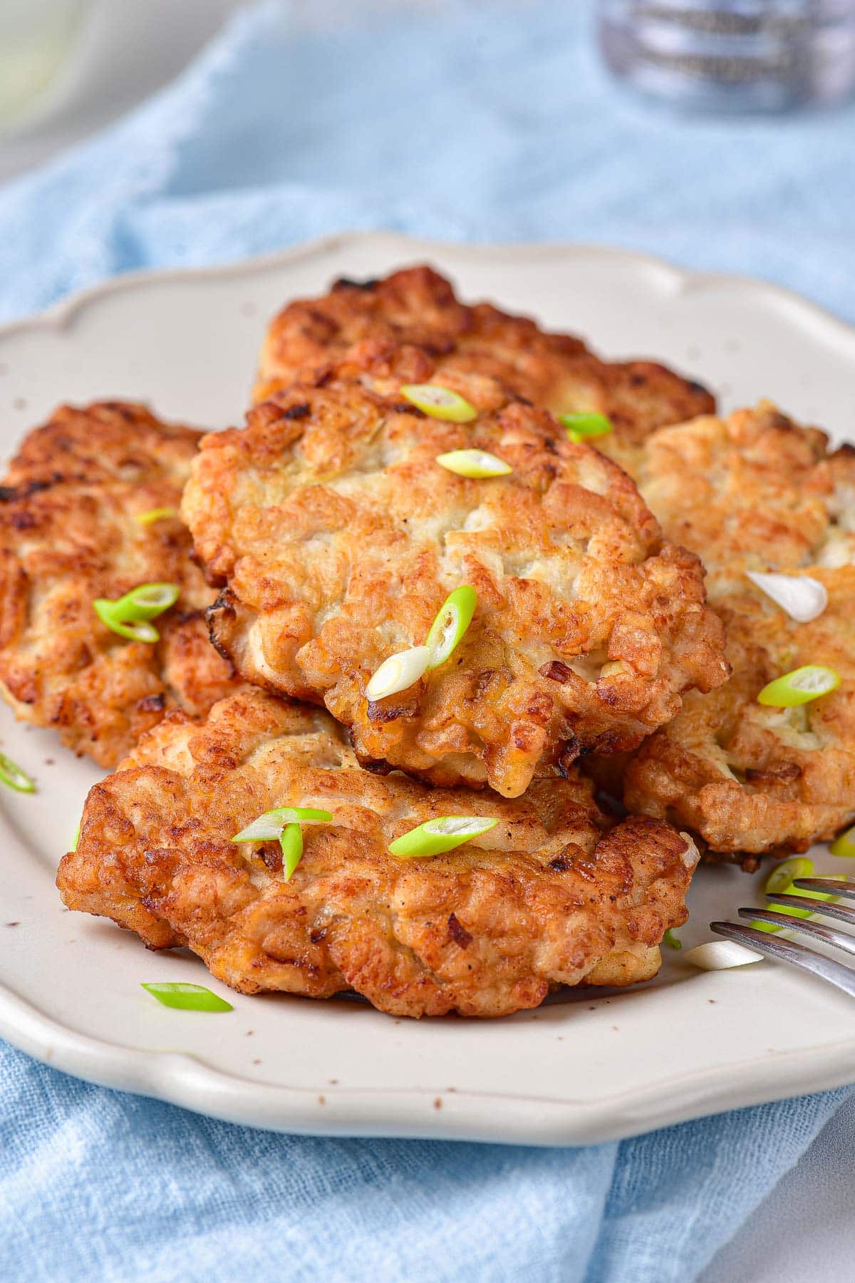 fried meat patties on white plate covered in chopped onions.