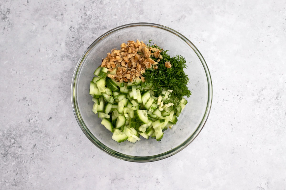 ingredients like chopped cucumber and dill in clear glass bowl on counter.