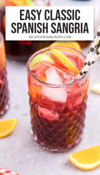 glass with red wine sangria, slices of fruit, ice, and paper straws plus text overlay "easy classic Spanish sangria".