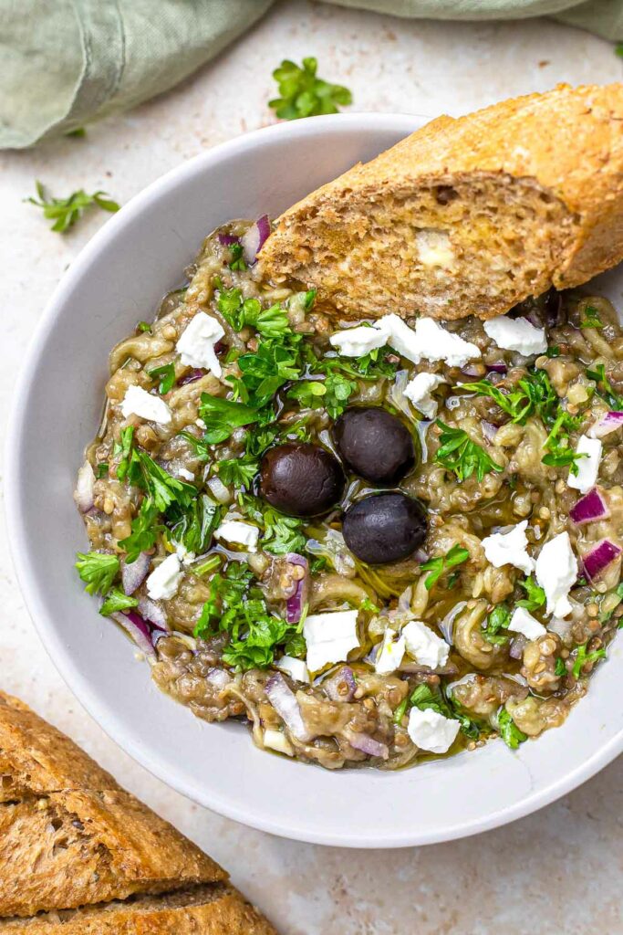 bowl of greek eggplant dip with feta and olives on top with bread on the side.