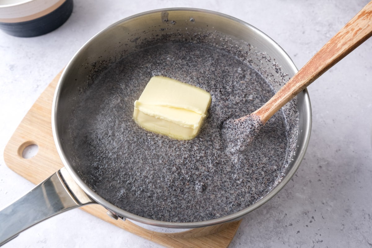 large chunk of butter in silver pot of poppy seed mixture with wooden spoon sticking out.
