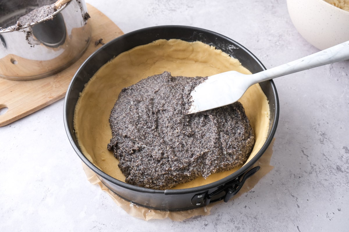 white spatula spreading poppy seed mixture into pan with raw crust on the bottom.