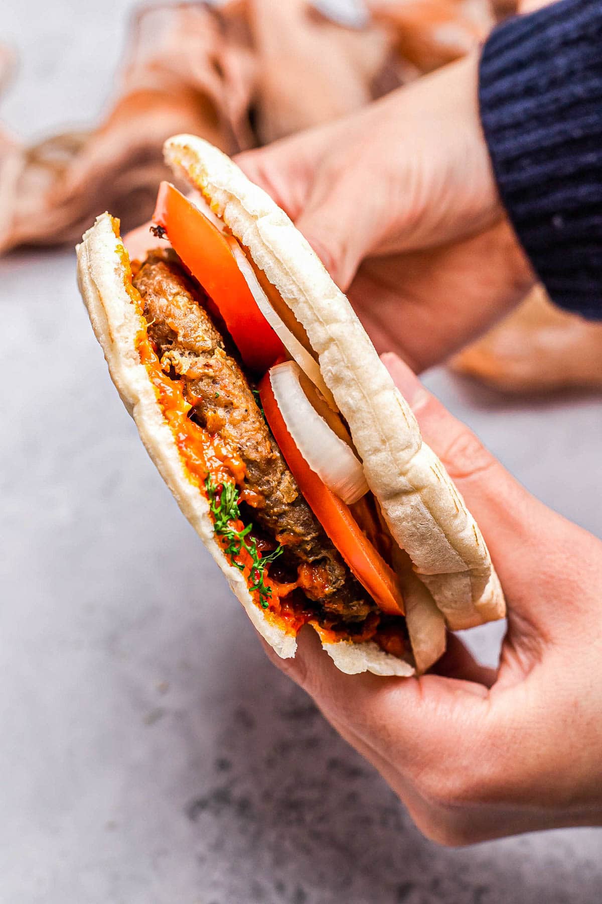 hand holding serbian burger in flatbread with tomatoes and onion.
