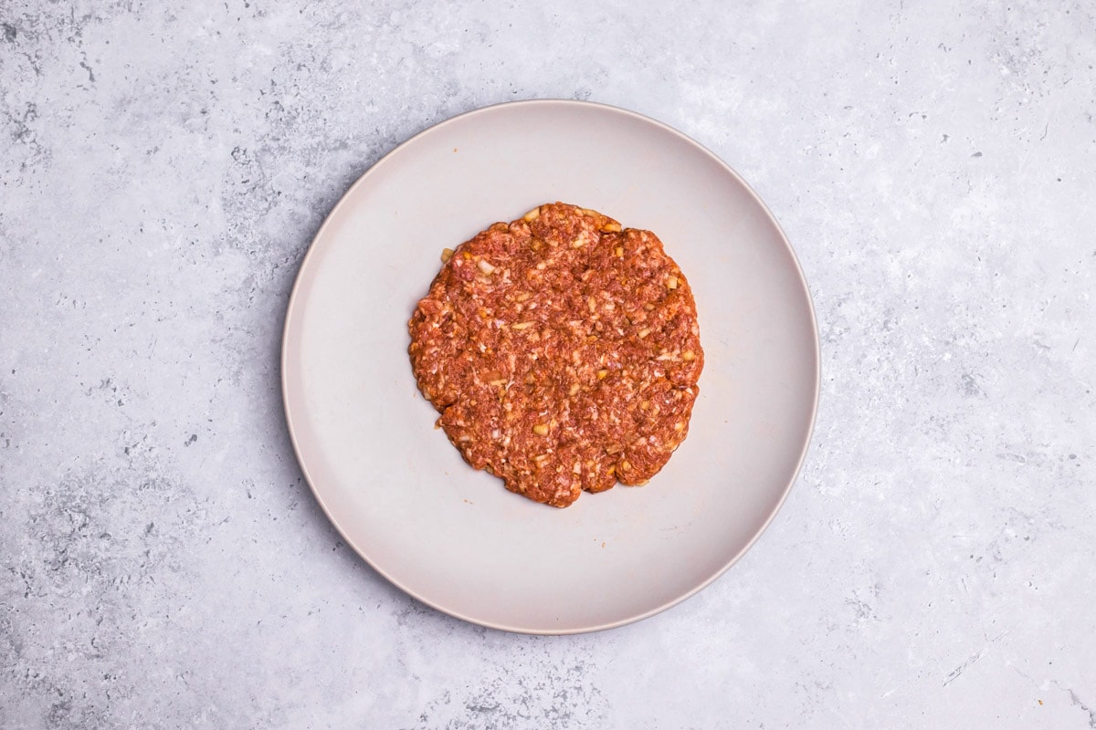 round raw meat patty laying on large plate on counter.