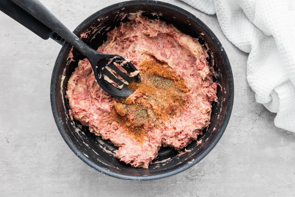 creamy beef blend in frying pan with spices sitting on top and black spatula.