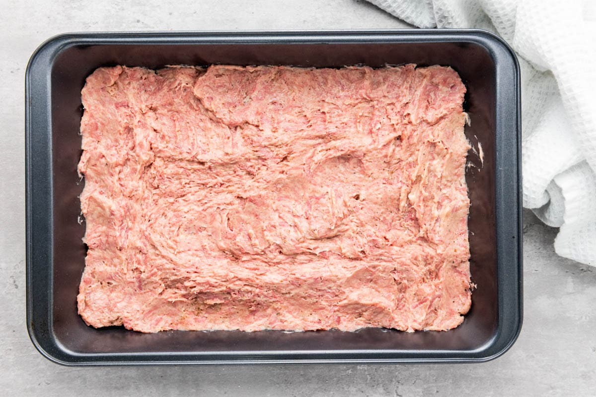 pink colored meaty mixture spread out in baking sheet.