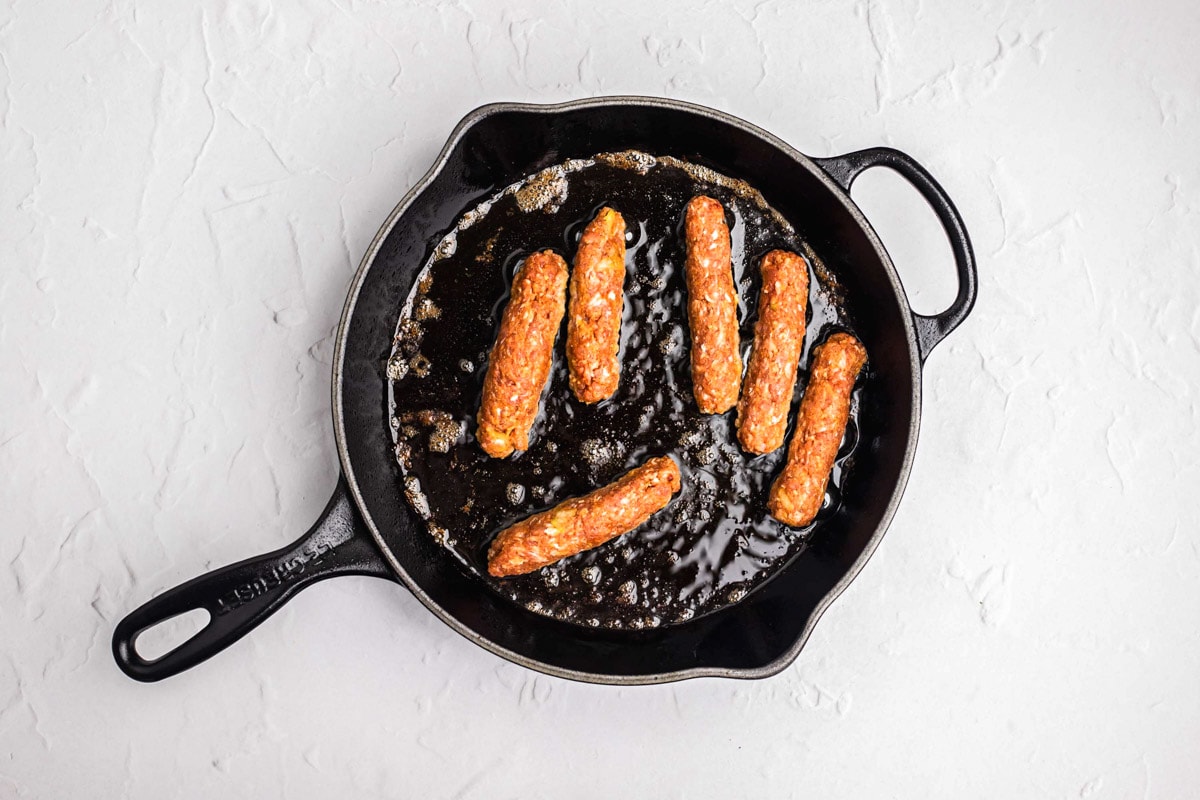frying cevapi sausages in oil in black cast iron pan.