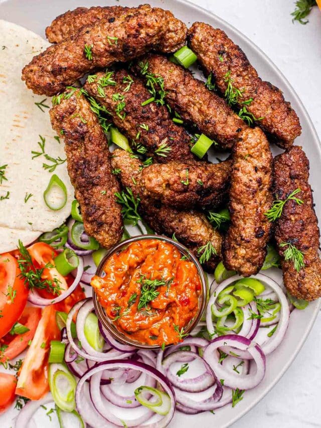 cooked cevapi sausages on plate with onion and tomatoes.