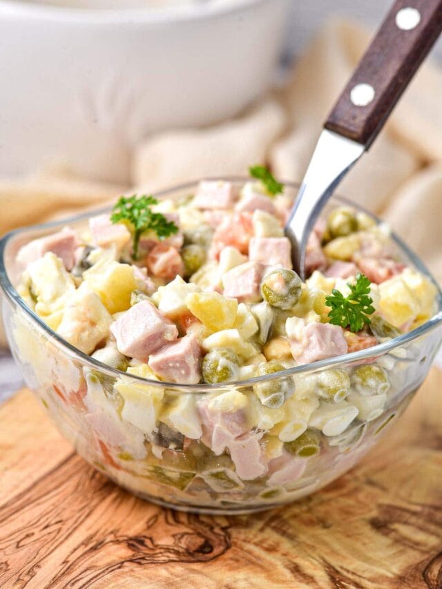 clear glass bowl of colorful olivier salad with brown spoon handle sticking out.