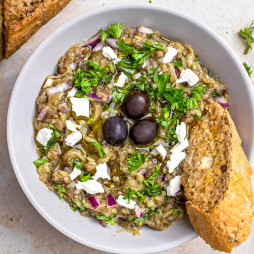 bowl of eggplant dip with olives on top and bread on the side.