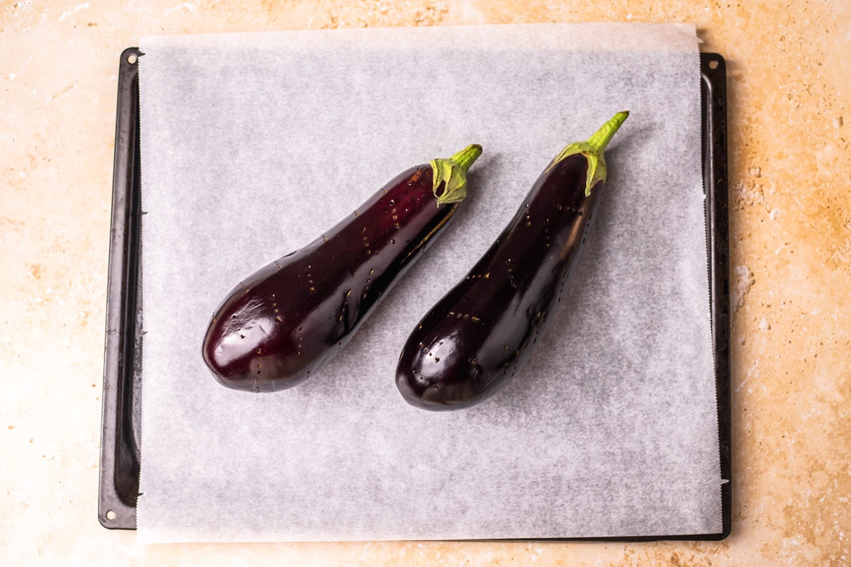 raw whole eggplants on parchment paper on baking sheet.