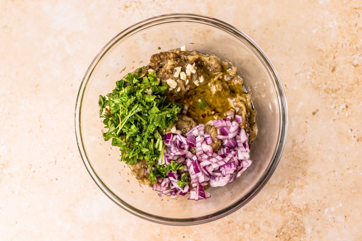 chopped onion and parsley in clear glass bowl with mashed eggplant.