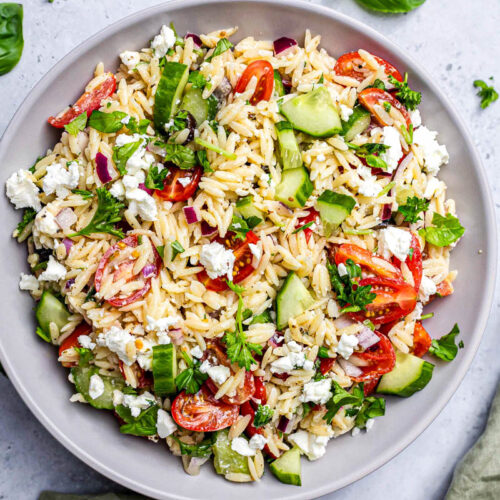 large bowl of colorful orzo salad with basil leaves and green cloth beside.