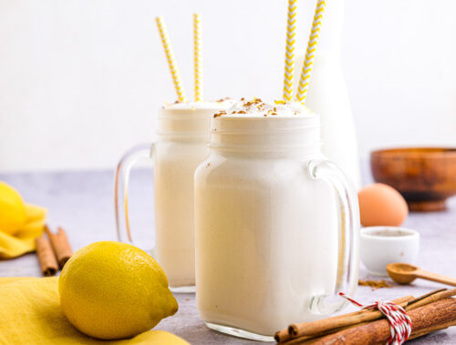 two mason jars of filled with white spanish milkshake with lemons and cinnamon around.
