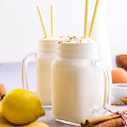two mason jars of filled with white spanish milkshake with lemons and cinnamon around.