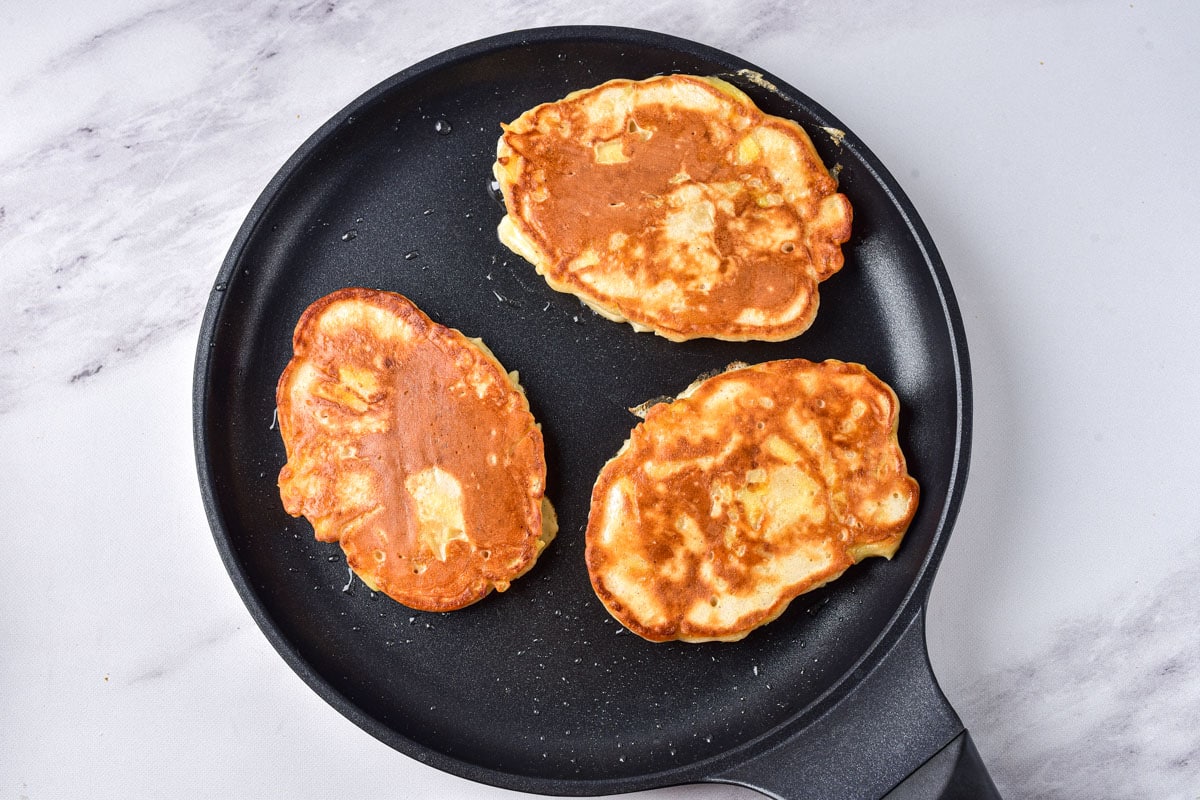 fried apple pancakes in black pan with grey counter around.