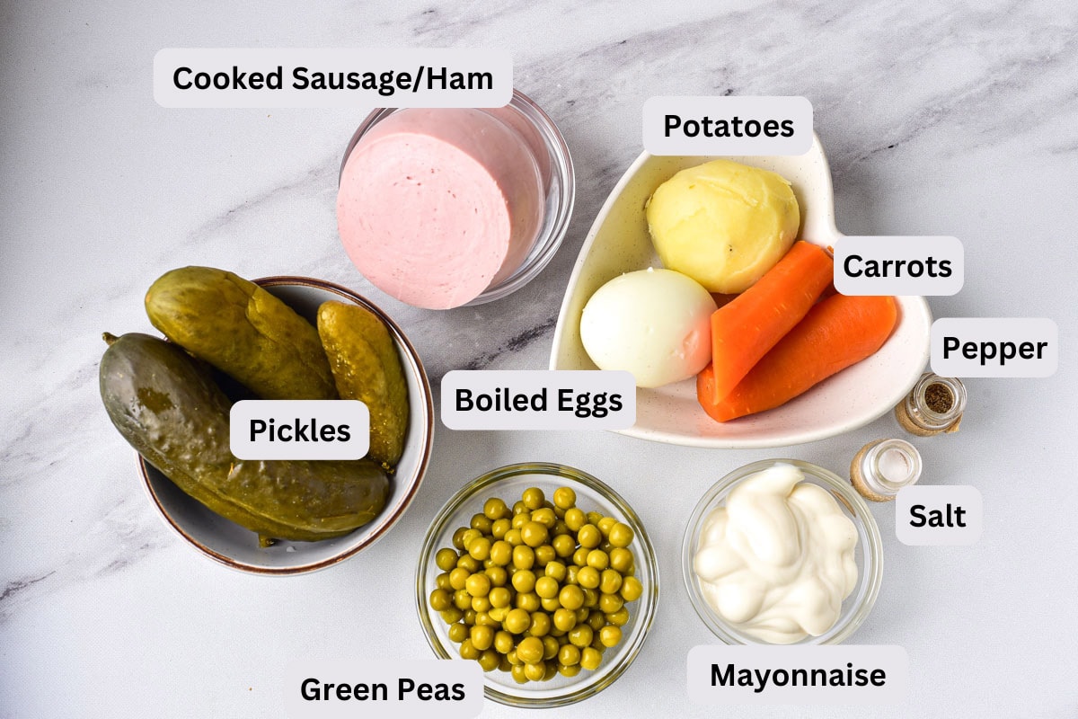 ingredients like potatoes, pickles, and peas in clear glass bowls with labels on marble counter.