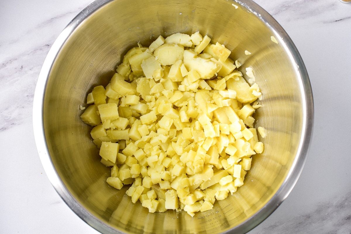 chopped cooked potatoes in silver mixing bowl on counter.