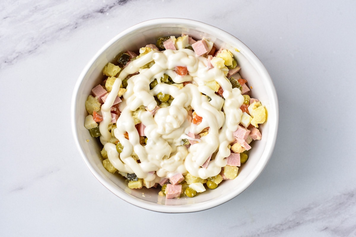 russian potato salad with mayo on top not mixed in sitting in white bowl with grey counter around.