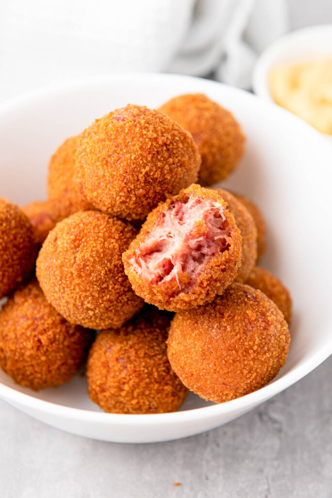 bite out of fried dutch bitterballen sitting on top of other balls in white bowl.