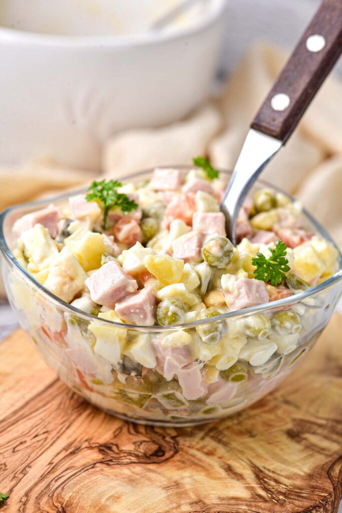 clear glass bowl of colorful olivier salad with brown spoon handle sticking out.