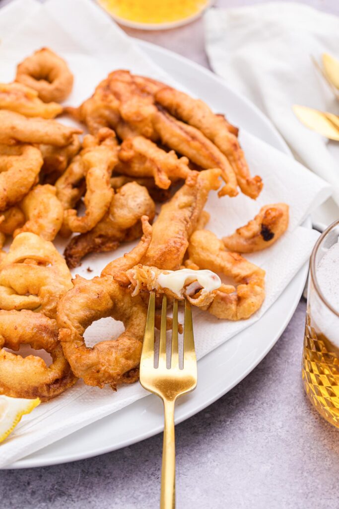 fried calamari rings on plate with golden fork piercing one piece with mayo on it.