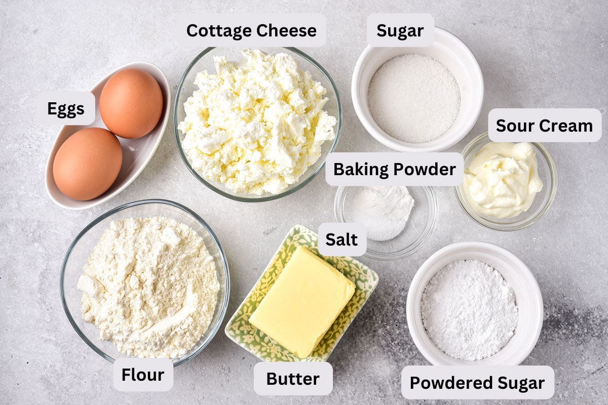 bowls of baking ingredients like flour and butter on grey counter with labels seen from above.