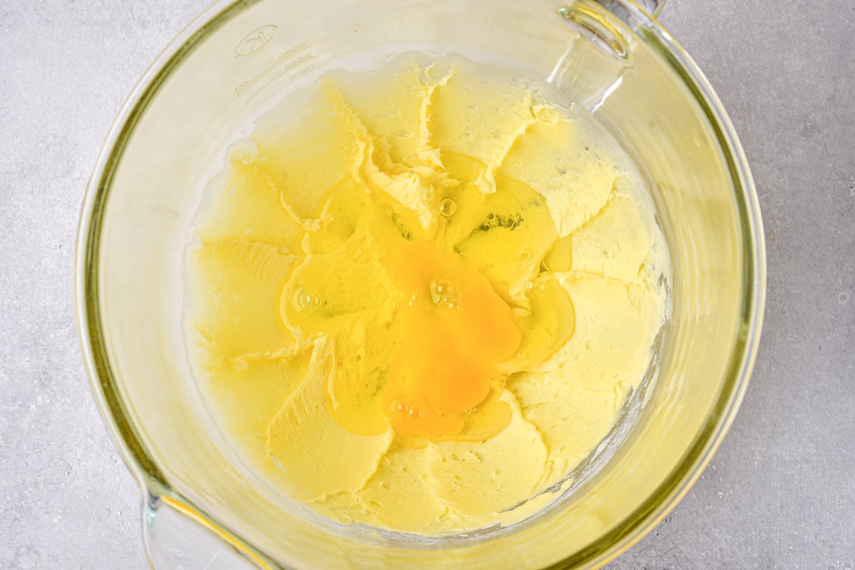 butter mixture in glass bowl with raw eggs cracked into the middle.
