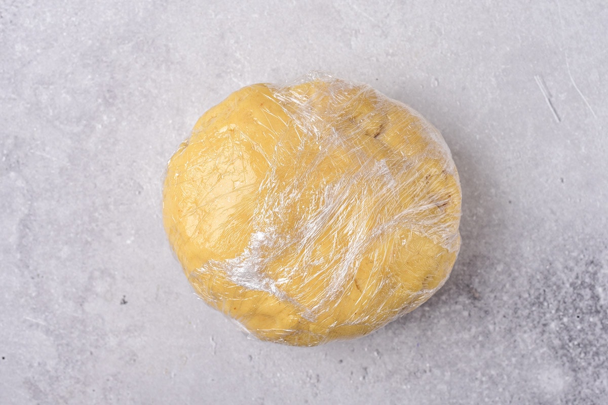 ball of pastry dough wrapped in cling film sitting on grey counter.