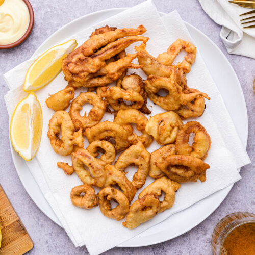round plate of fried calamari with lemon wedge beside on counter.