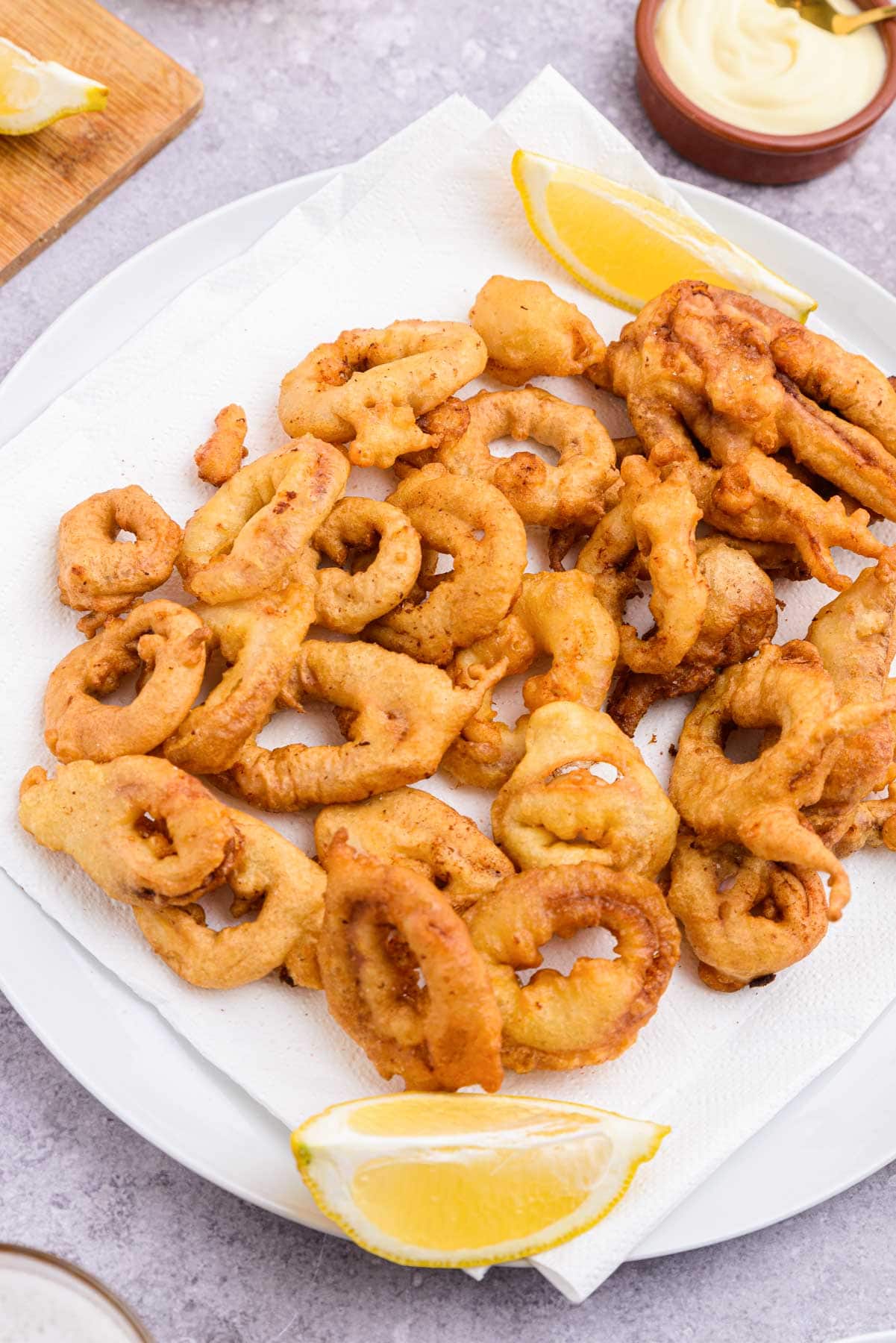 plate covered in fried calamari rings with lemon wedge in front.