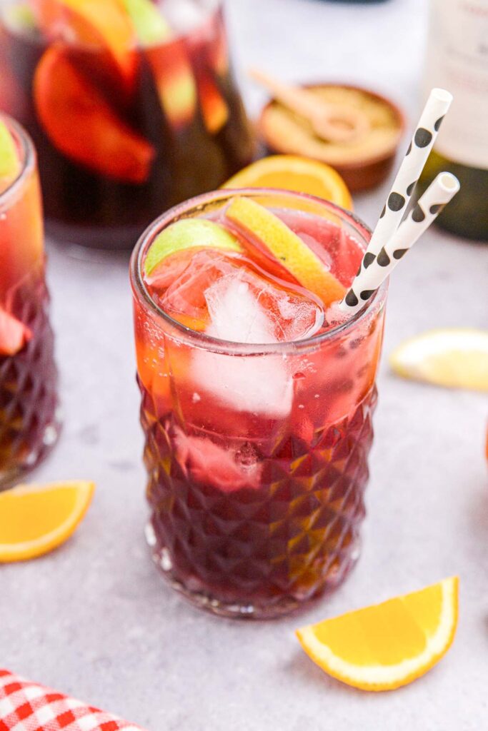 tall clear glass of red sangria with lemon wedge beside on counter.