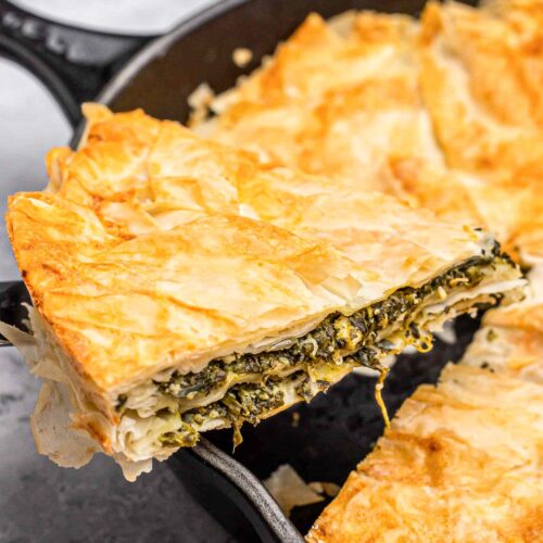 slice of spinach-filled burek being lifted from black cast iron pan.