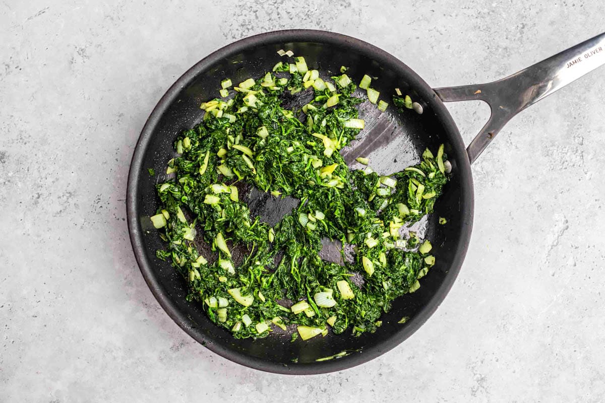 green spinach frying in black cast iron pan with grey counter around.