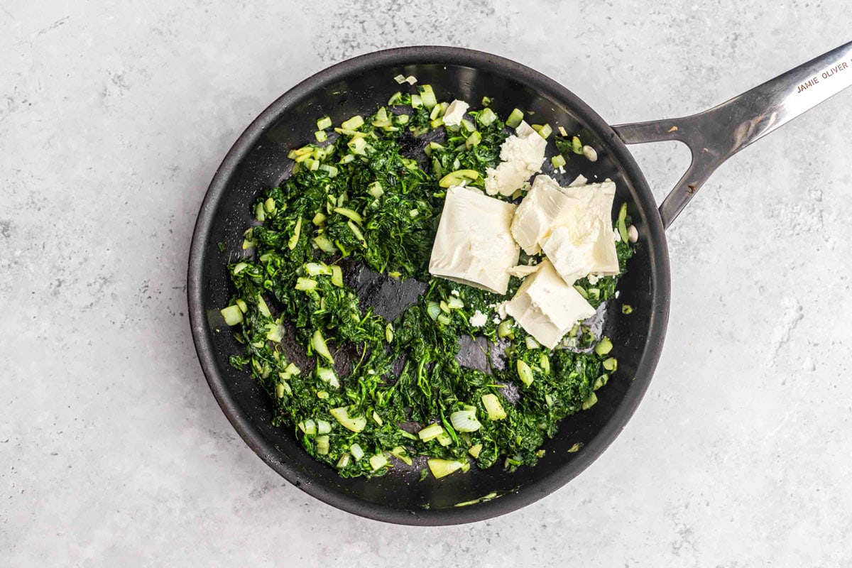 spinach and feta cheese frying in black cast iron pan on counter.