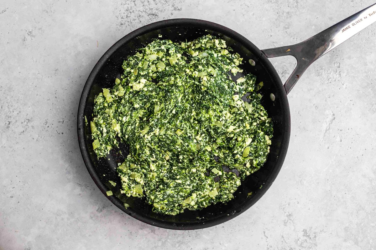 a cheesy spinach mixture sitting in black cast iron pan with grey counter around.