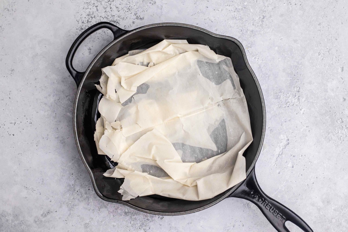 phyllo sheets laying in bottom of black cast iron pan with grey counter around.