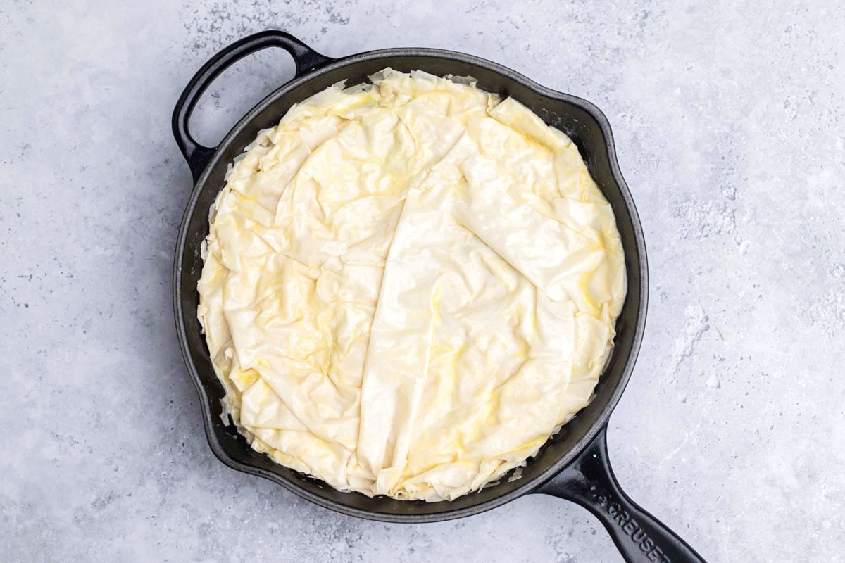 sheets of raw phyllo dough layered in black cast iron pan with grey counter around.